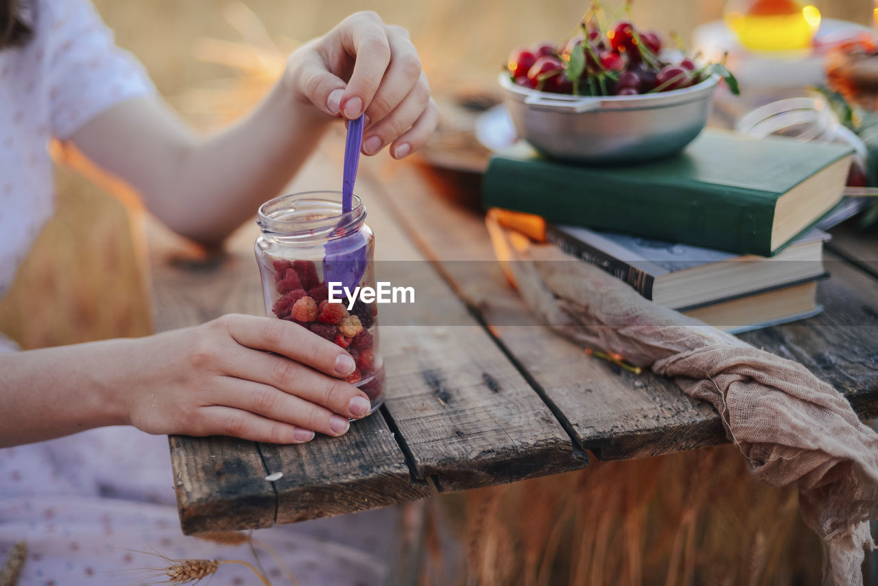 Midsection of woman eating berry fruits while sitting at wooden table