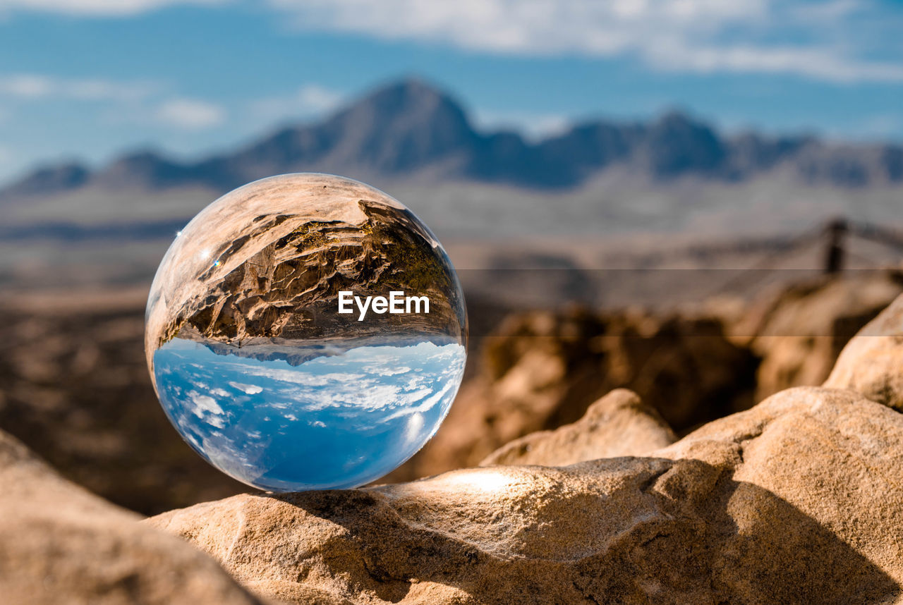 CLOSE-UP OF CRYSTAL BALL ON ROCKS AGAINST SKY