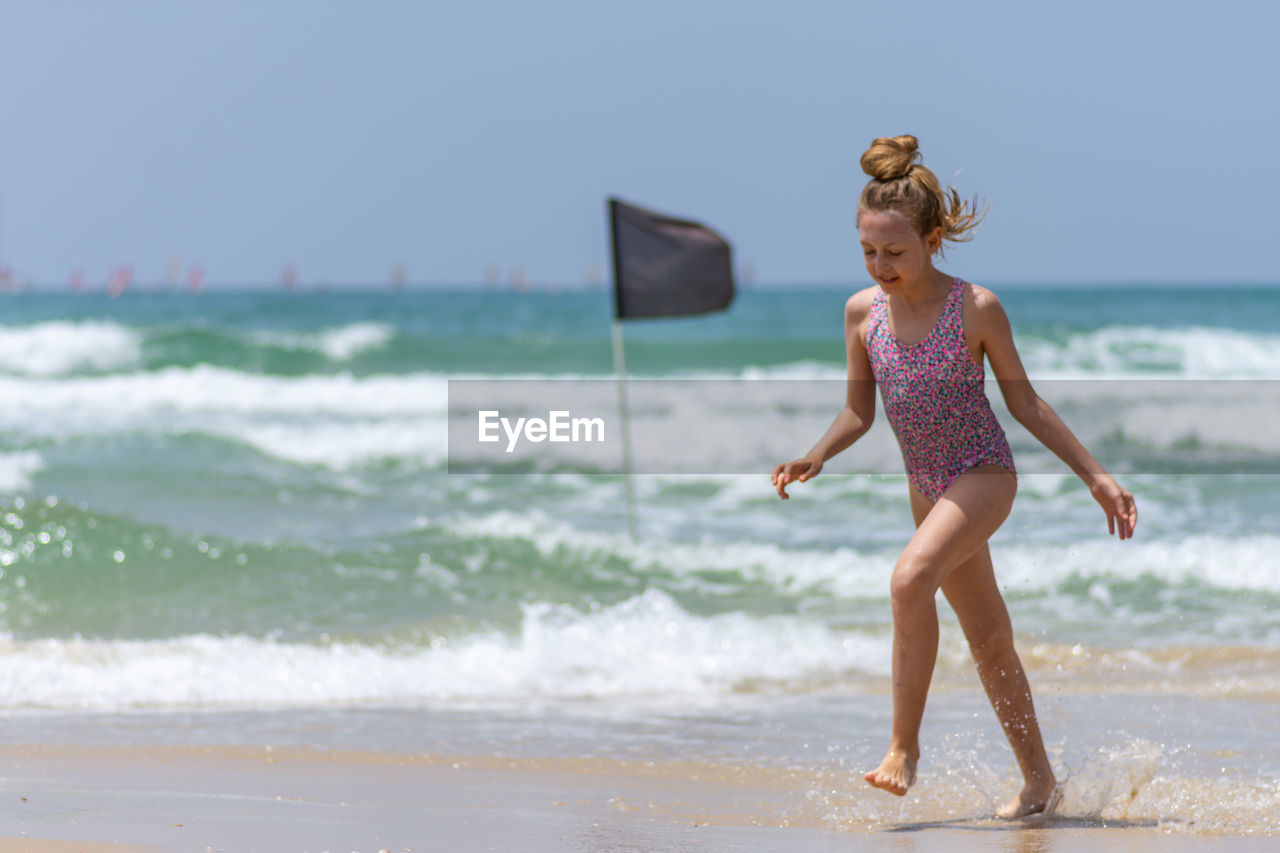 Full length of girl walking on shore at beach against sky during summer