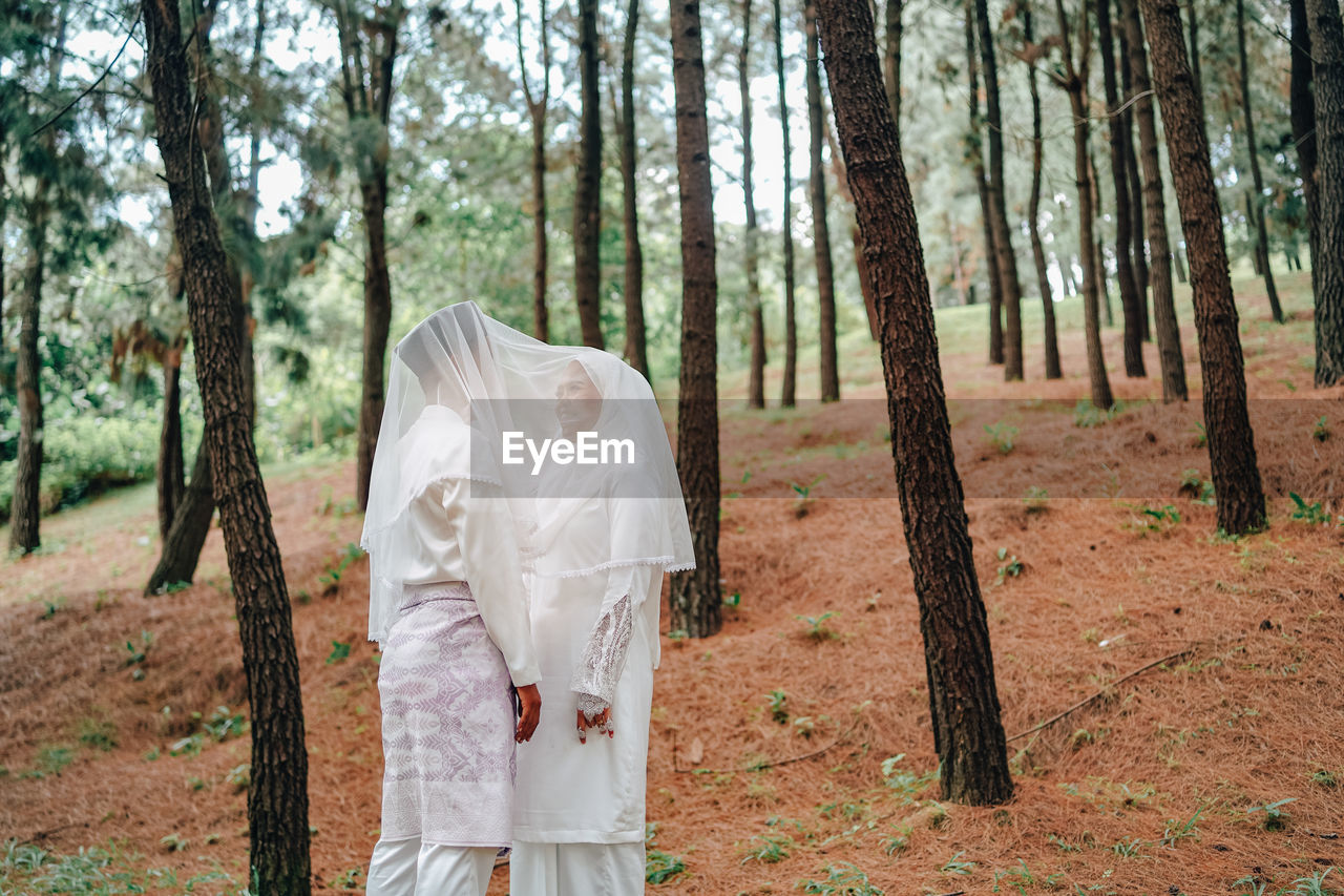 Bride and bridegroom standing amidst trees in forest