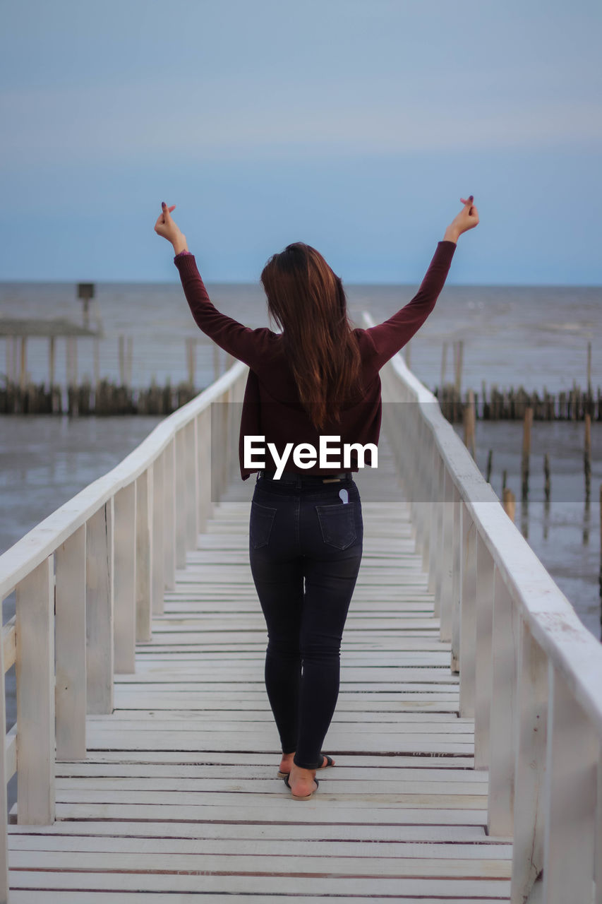 FULL LENGTH REAR VIEW OF WOMAN STANDING AGAINST RAILING