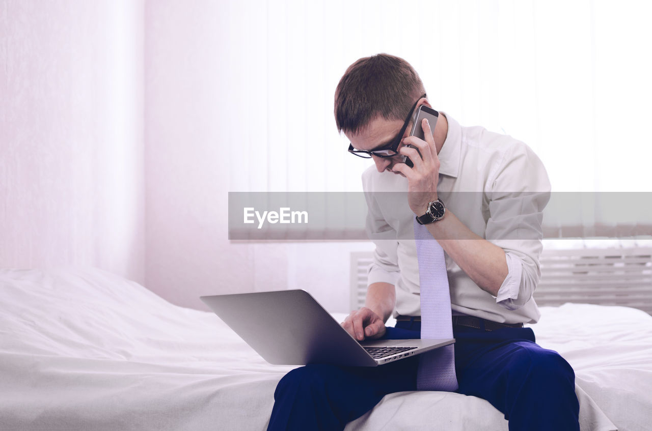 Businessman talking on mobile phone while working on laptop at home