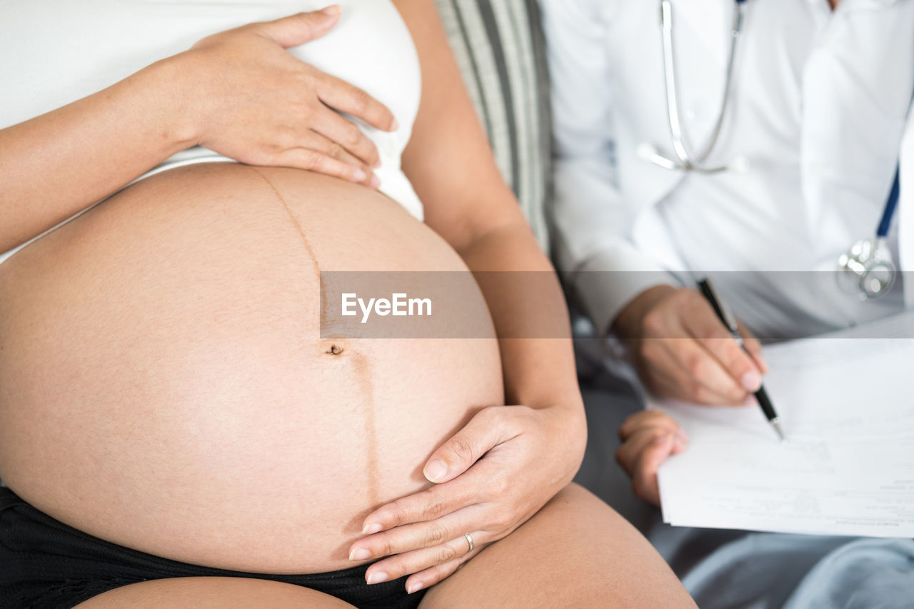 Midsection of pregnant woman sitting with female doctor in hospital