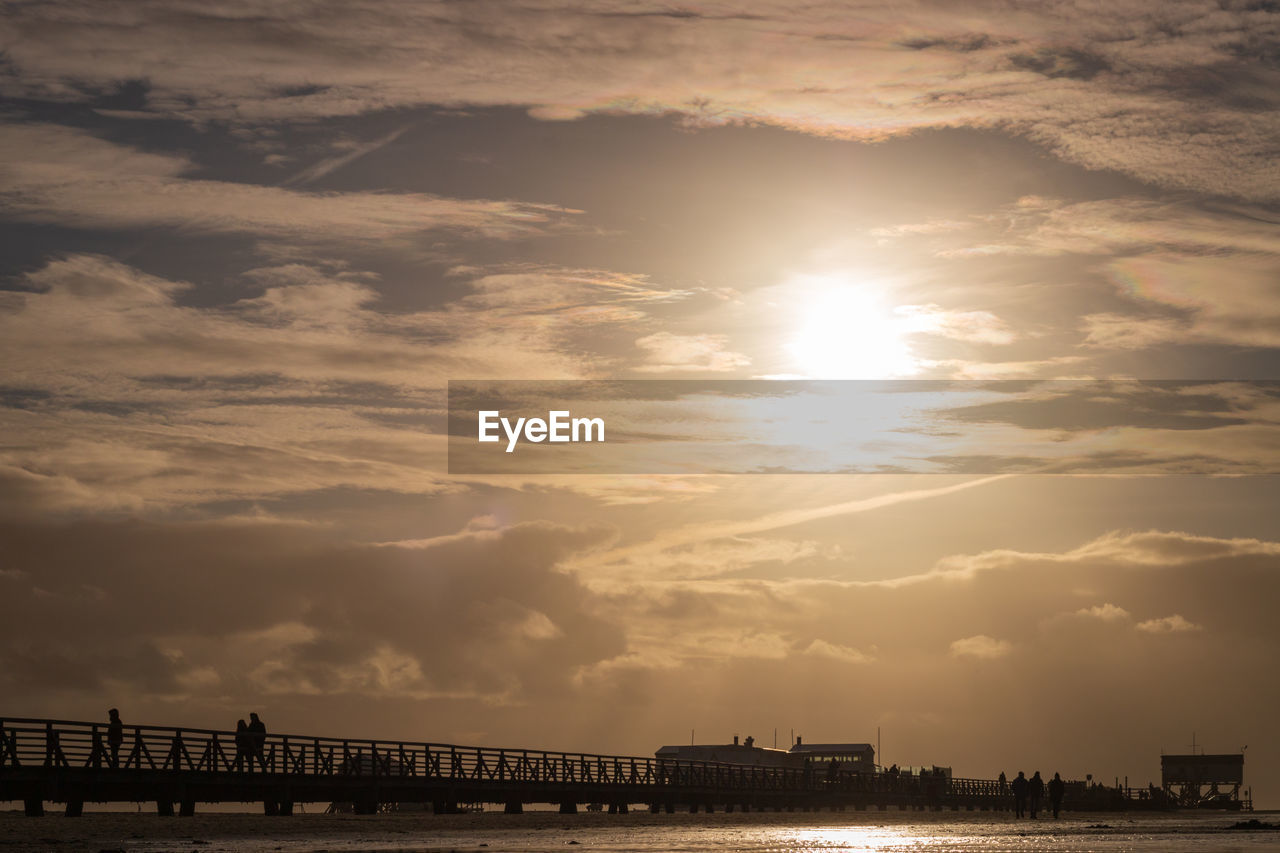 Silhouette pier over low tide wadden sea against sky during sunset