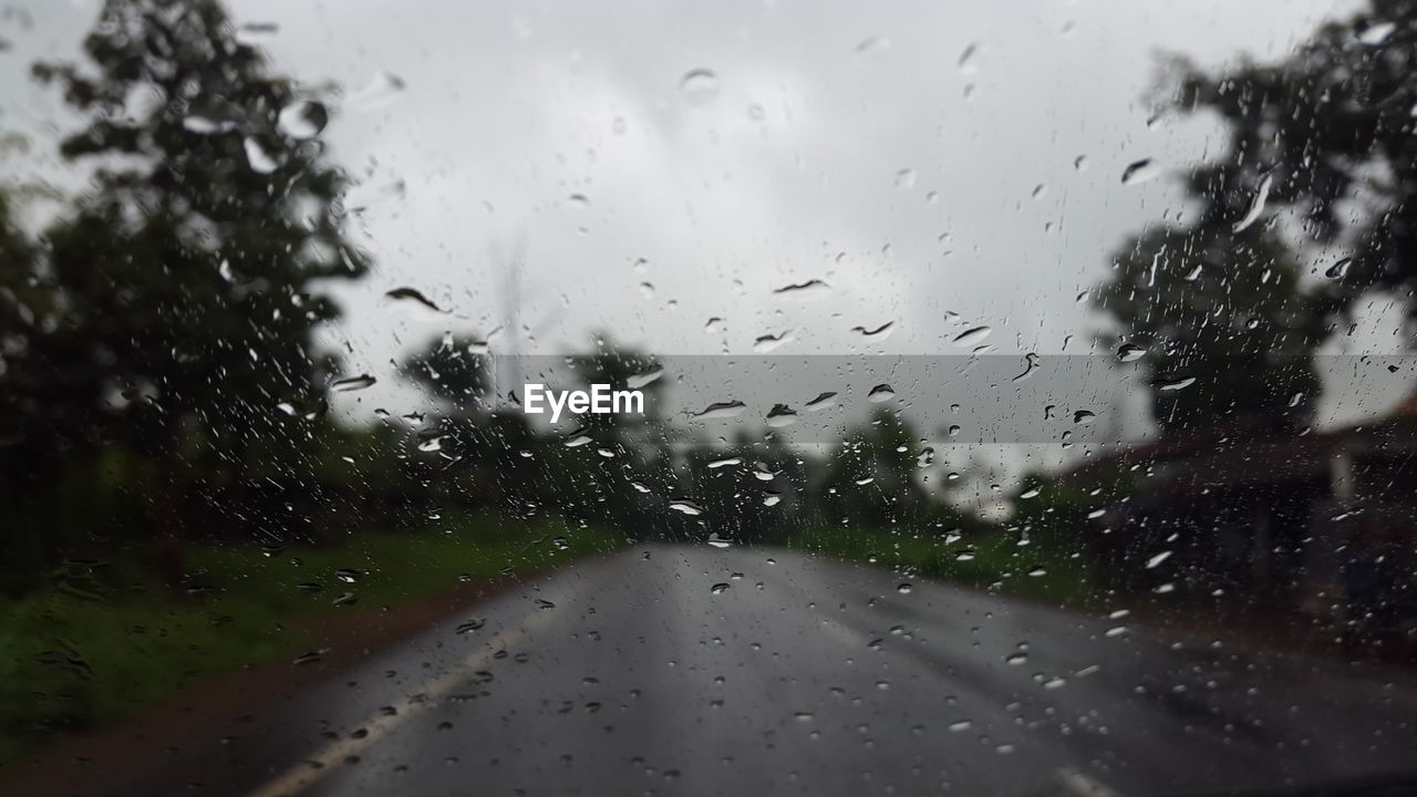 SURFACE LEVEL OF WET ROAD AGAINST CLOUDY SKY SEEN THROUGH GLASS WINDOW