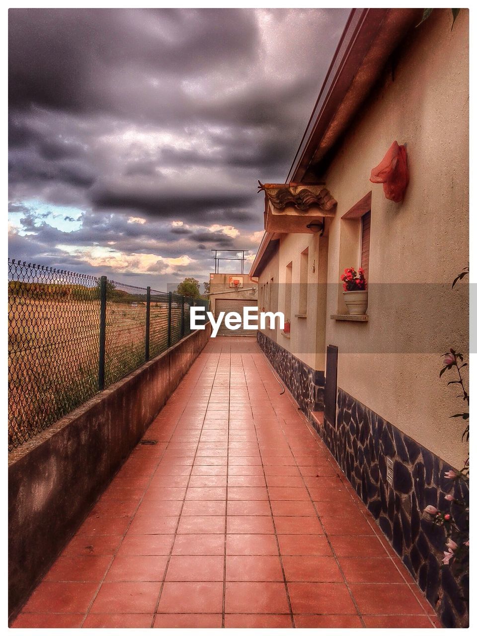 WALKWAY LEADING TOWARDS BUILDING AGAINST CLOUDY SKY