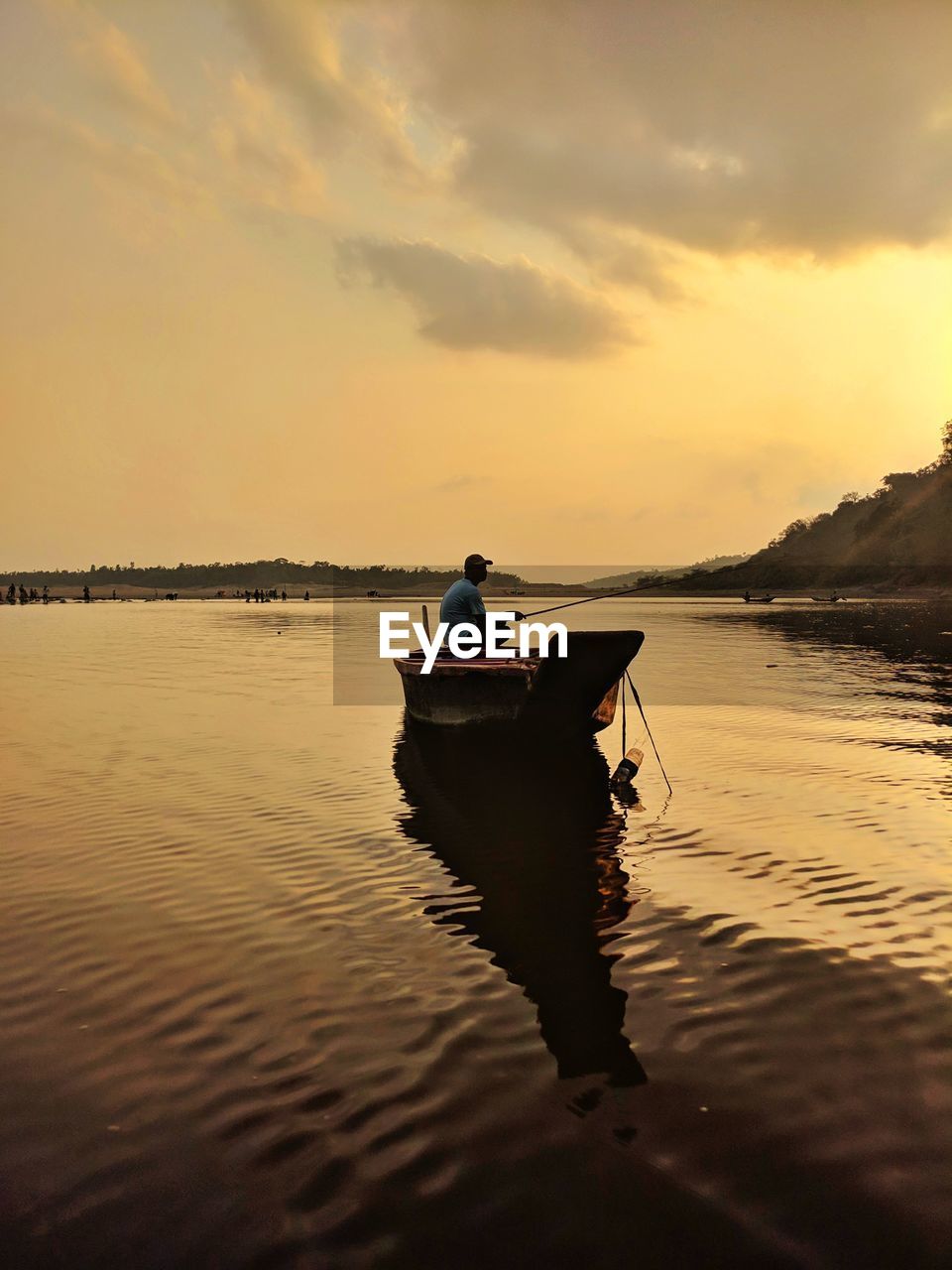 Man fishing while sitting on boat in lake against sky during sunset