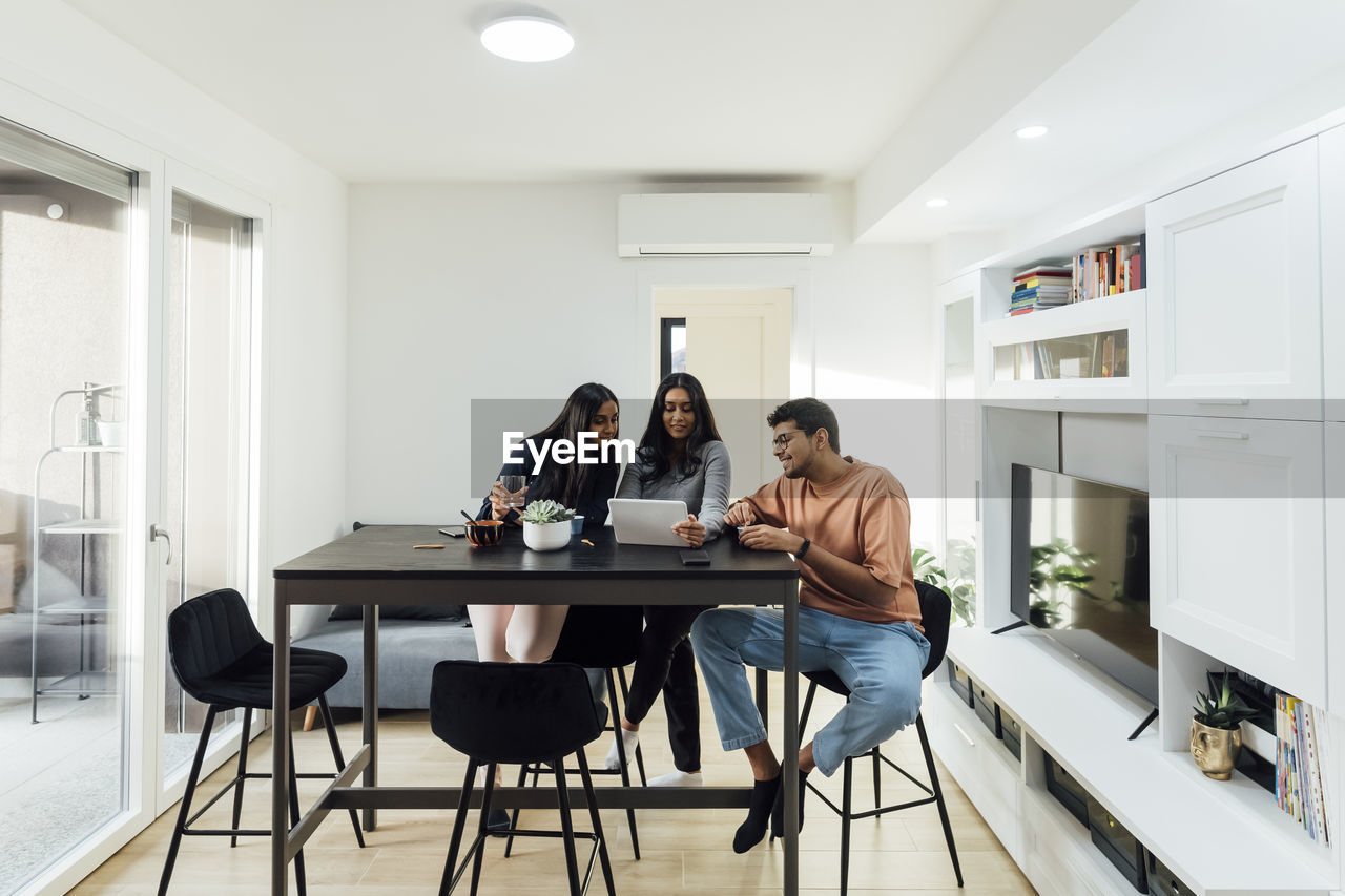 Young woman sharing tablet pc with man and woman at table in living room