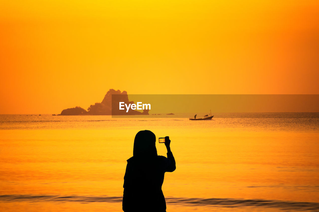 REAR VIEW OF SILHOUETTE MAN ON SEA AGAINST ORANGE SKY