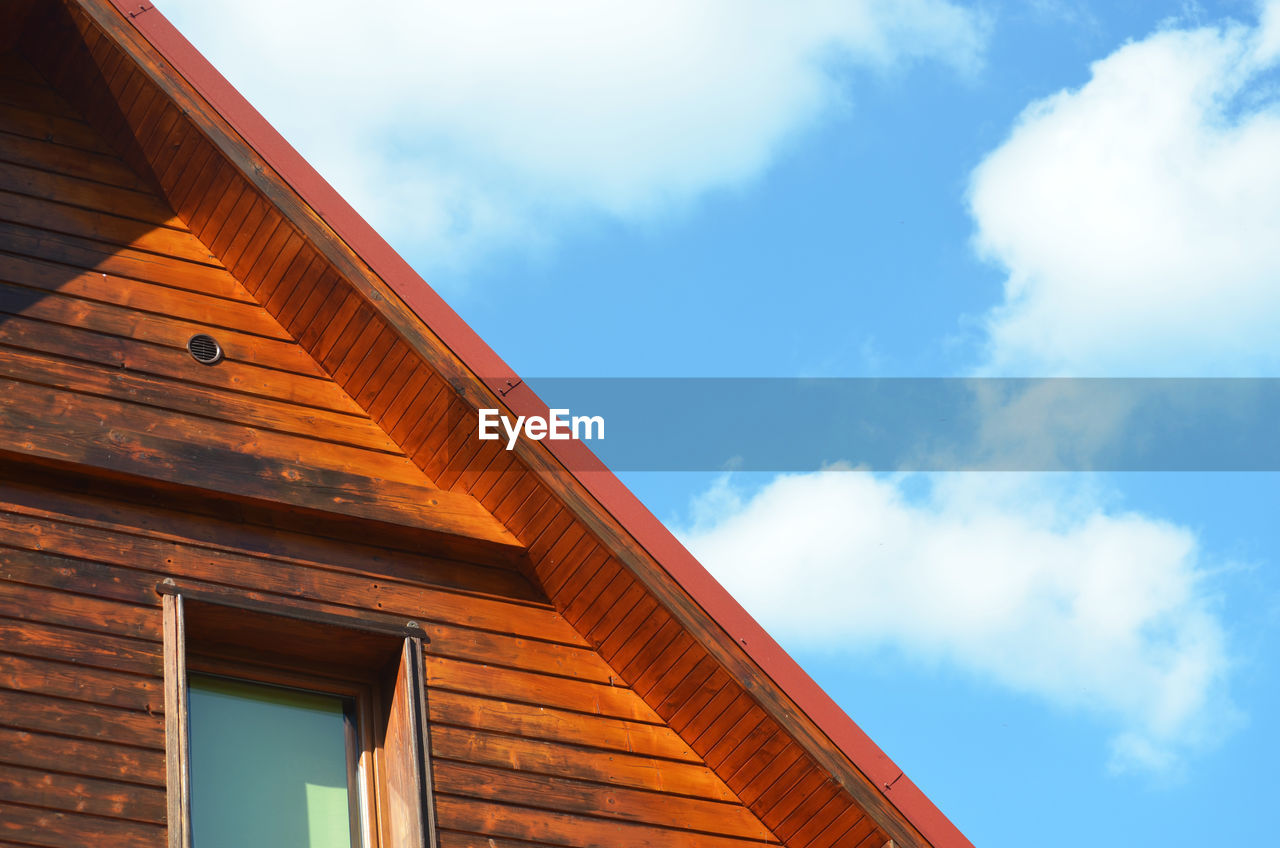 Piece of wooden house facade with window and pitched roof on the blue sky with cloudu background