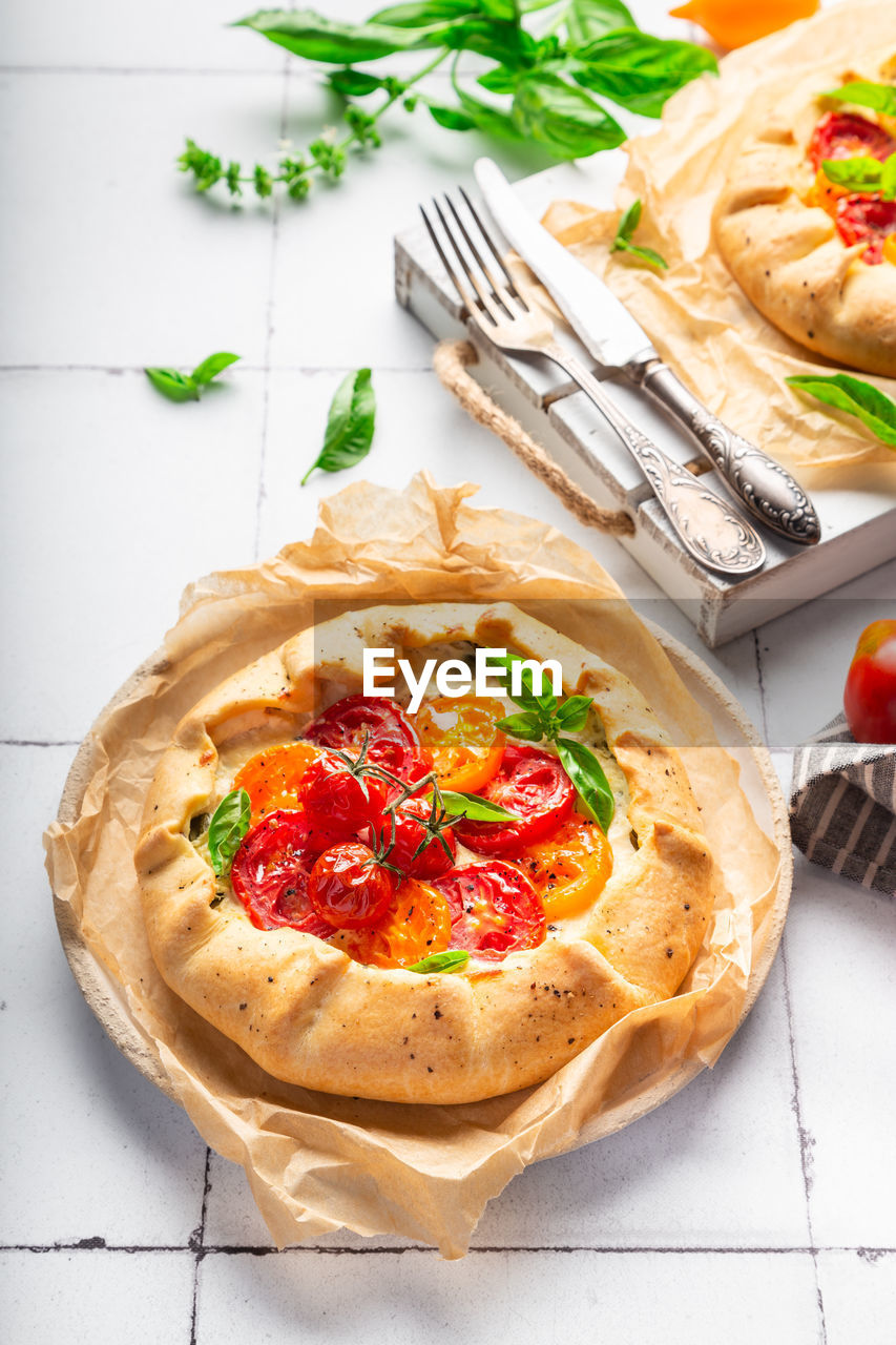 Fresh homemade galette with tomatoes, ricotta cheese and basil on white tile background.