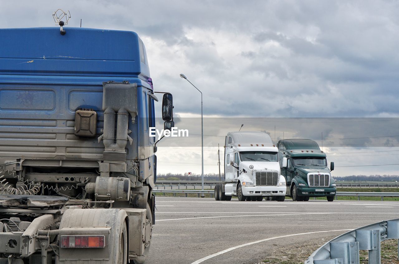 Trucks on road against cloudy sky