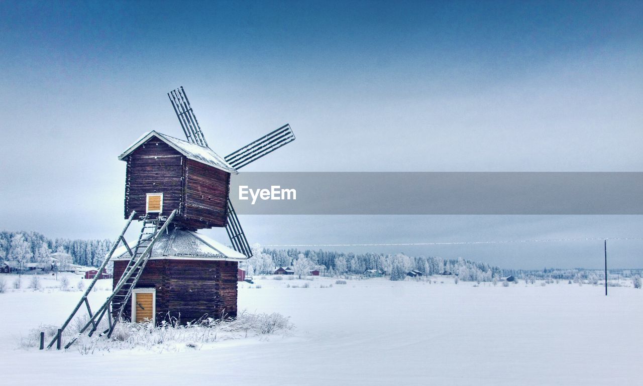 Traditional windmill on snow covered field against sky