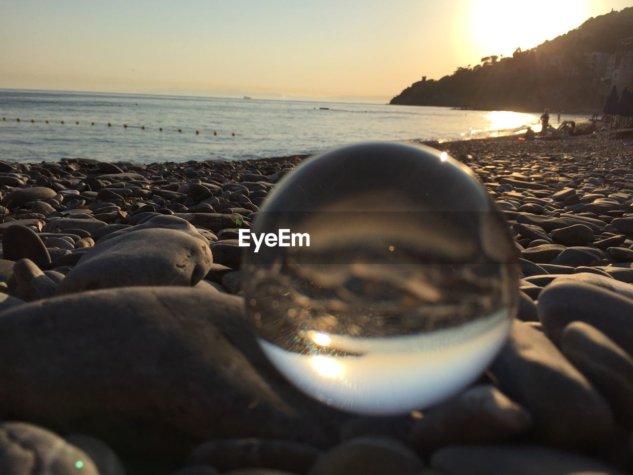 CLOSE-UP OF PEBBLES BY SEA AGAINST SKY DURING SUNSET