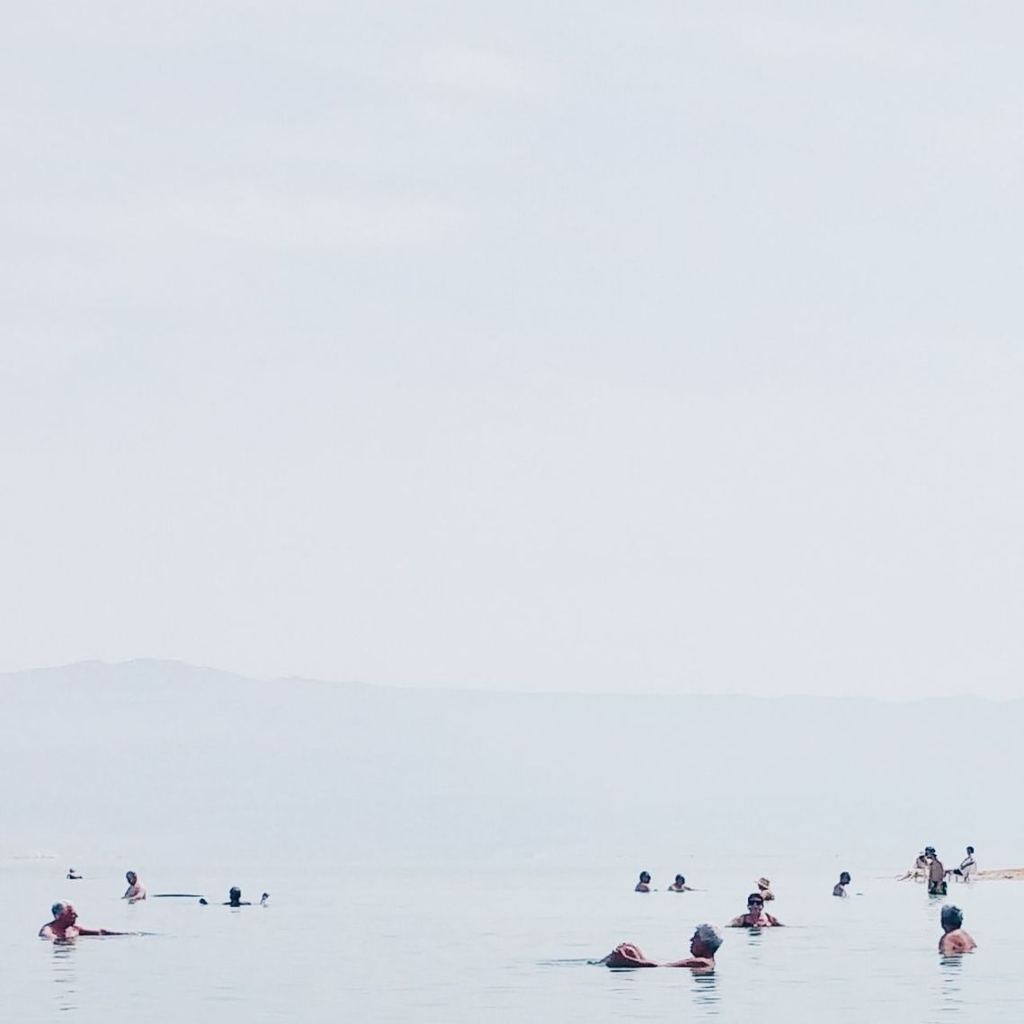People swimming in sea against clear sky during foggy weather