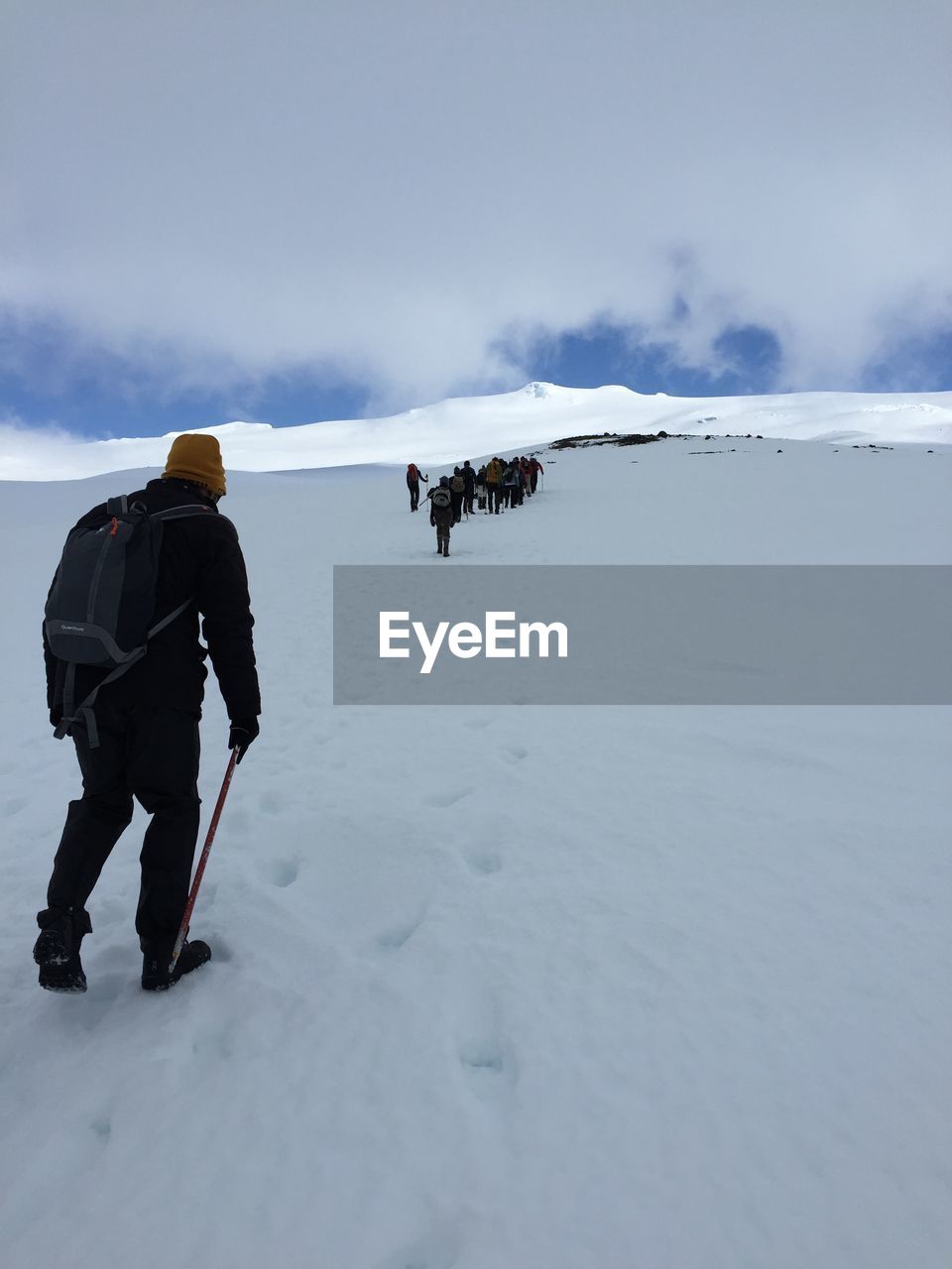 Rear view of hikers climbing uphill against cloudy sky