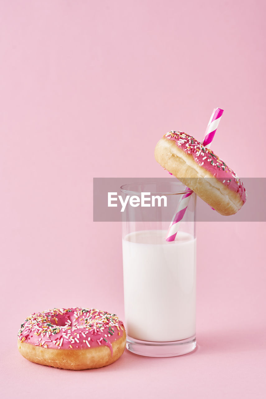 Donuts decorated with icing and sprinkle and glass of milk on pink background