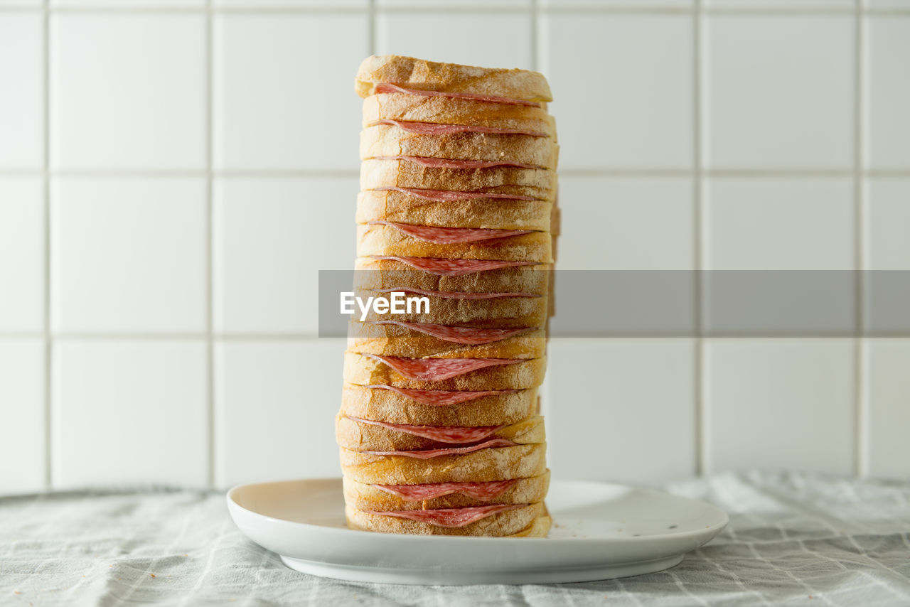 Close-up of bread stack with salami in plate on table