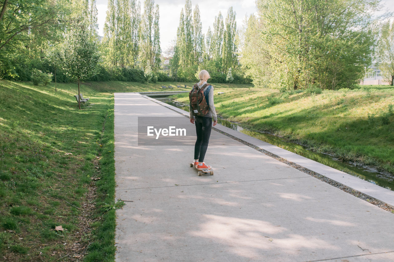 Rear view of woman skateboarding on footpath in park