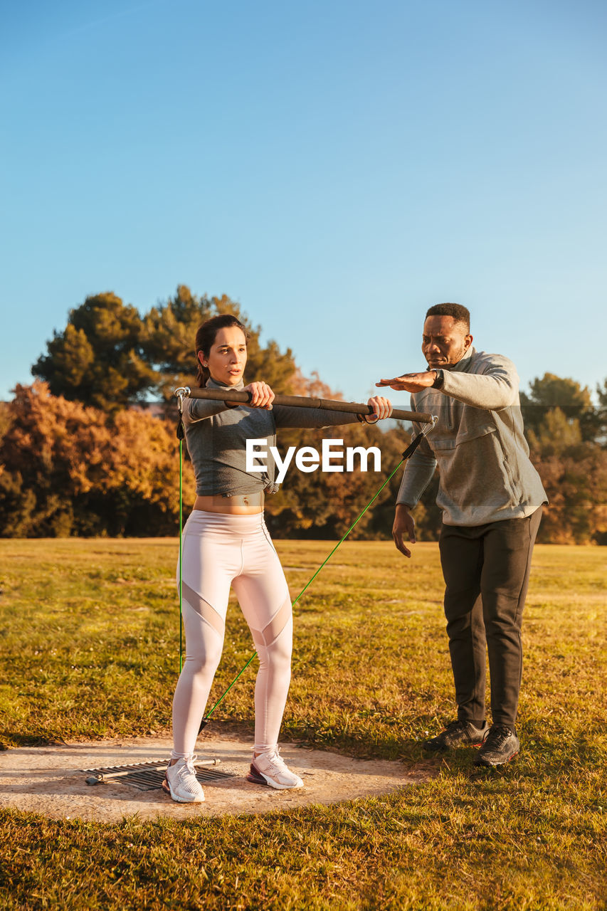 Woman pulling belt while instructor guiding on land against clear sky