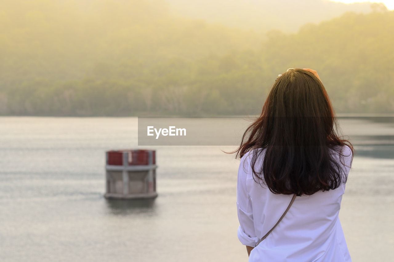Rear view of woman standing at riverbank against sky