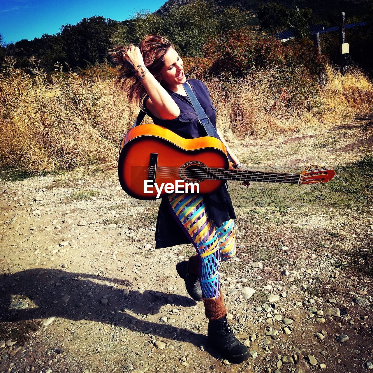 Woman with guitar walking on field