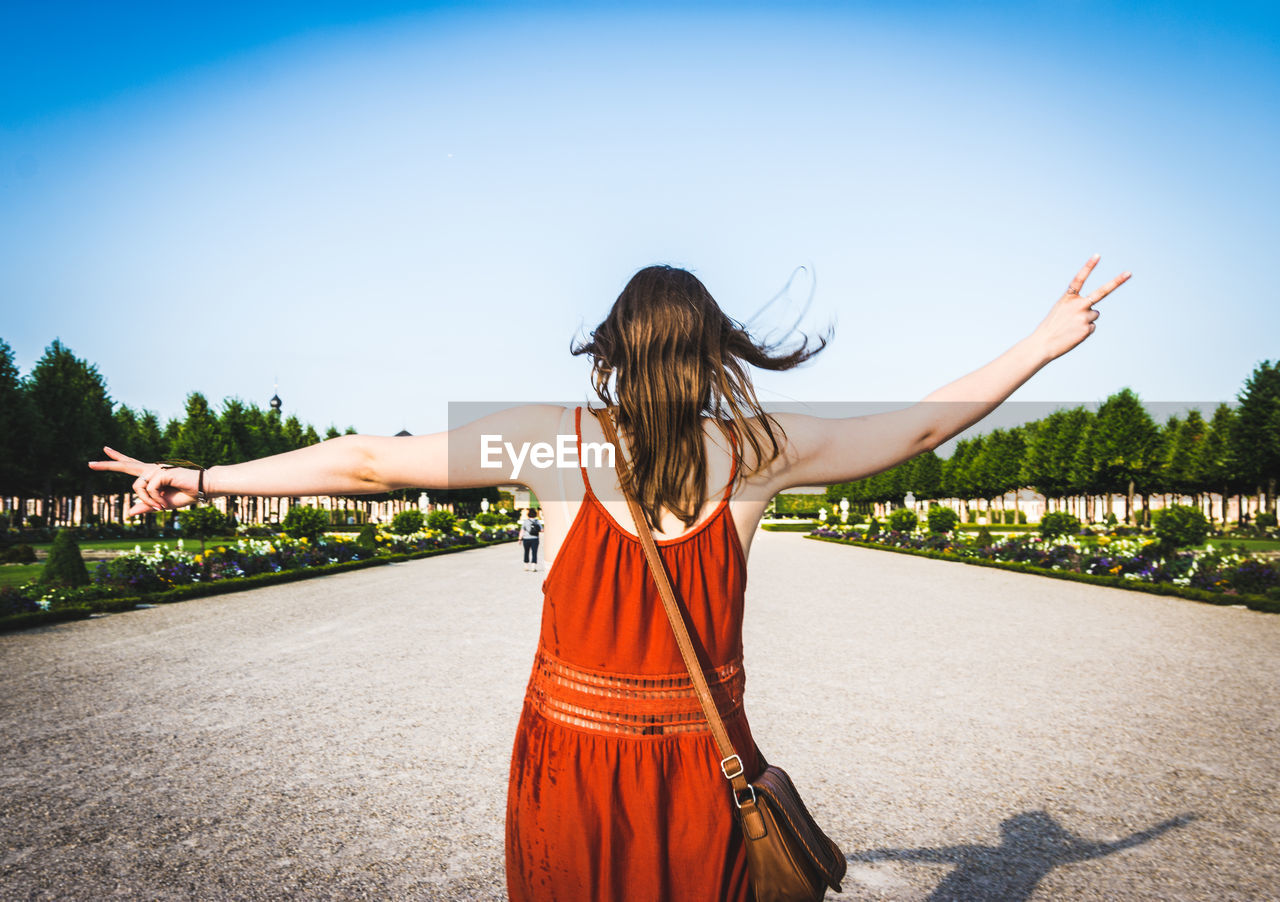 Rear view of woman gesturing while standing on road against sky