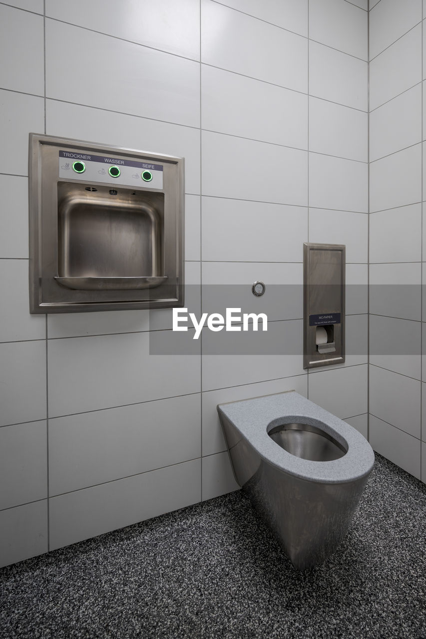 Interior of new and modern clean public restroom with white tiles and stainless steel bowl
