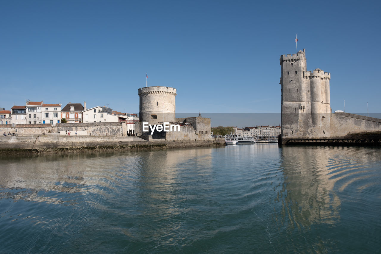 architecture, water, built structure, building exterior, sea, sky, building, travel destinations, clear sky, reflection, nature, tower, blue, history, the past, coast, travel, city, no people, waterfront, fort, day, lighthouse, tourism, outdoors, sunny, landmark, harbor, waterway, castle, land, copy space