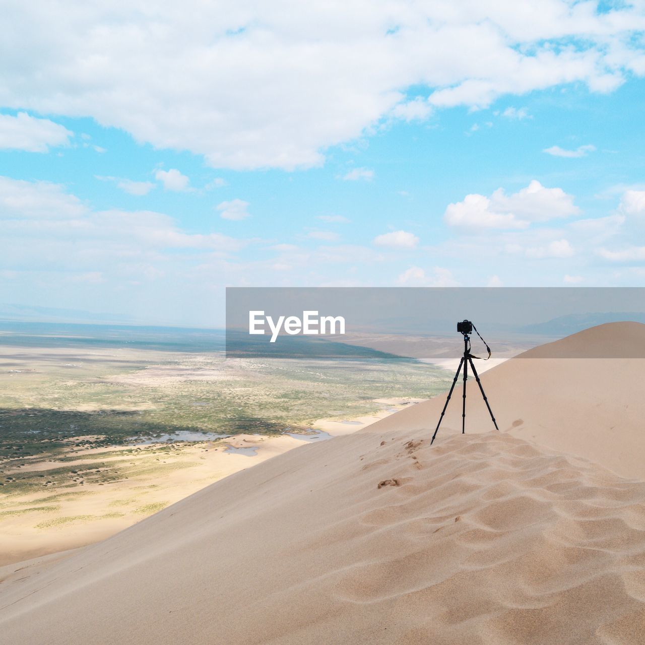 Tripod on sand in desert against cloudy sky during sunny day