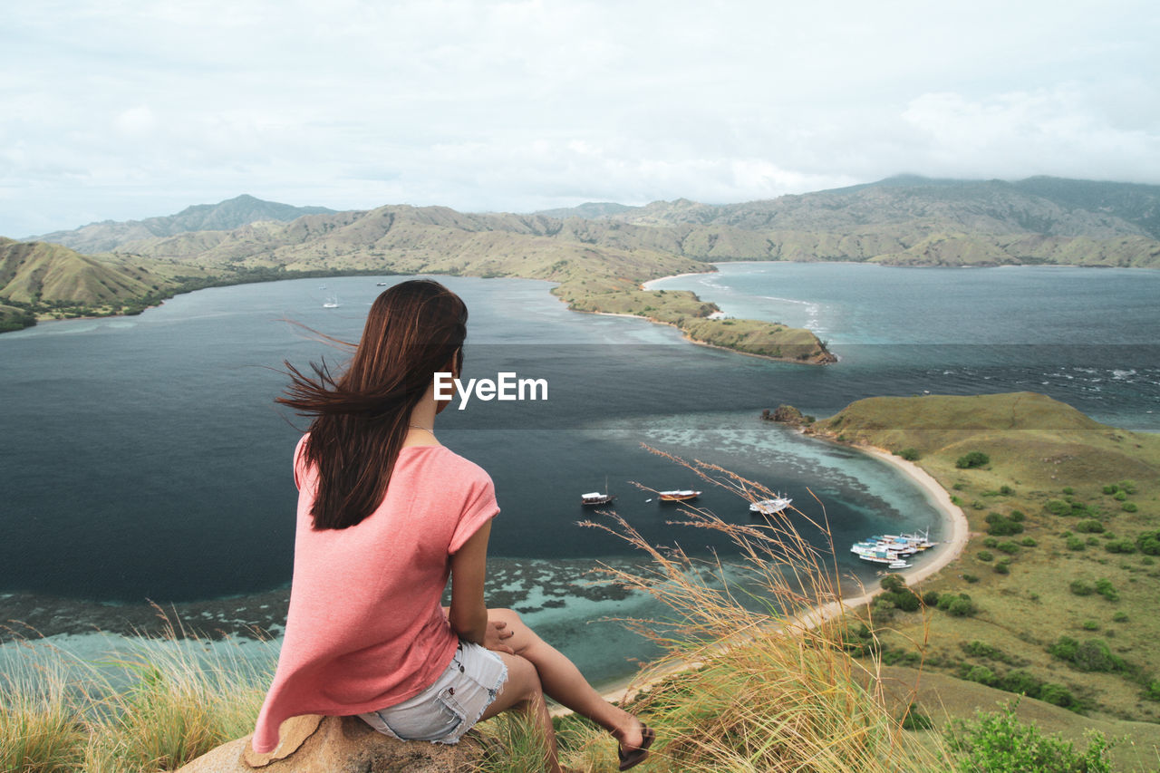 Rear view of woman sitting on mountain against sky