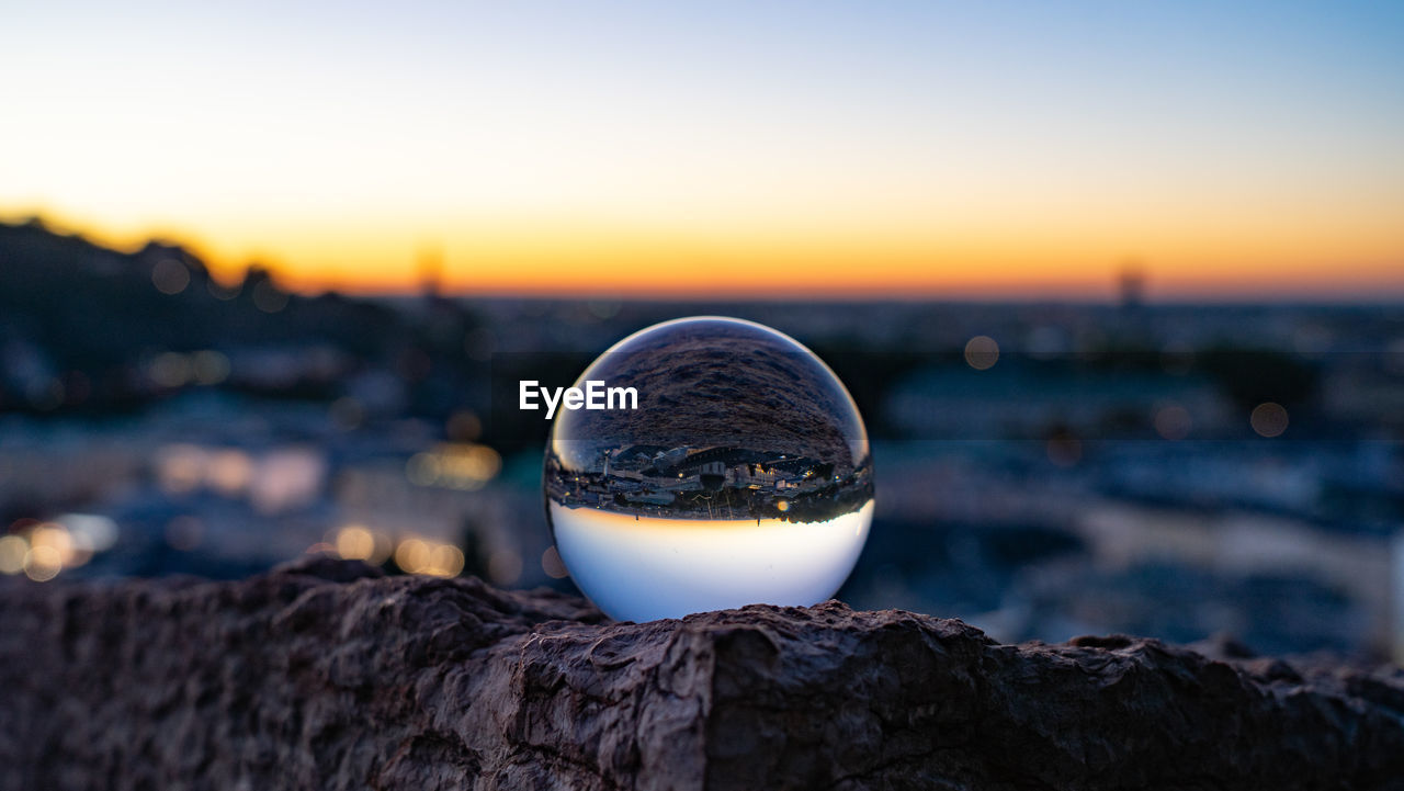 Close-up of crystal ball on rock against clear sky during sunset