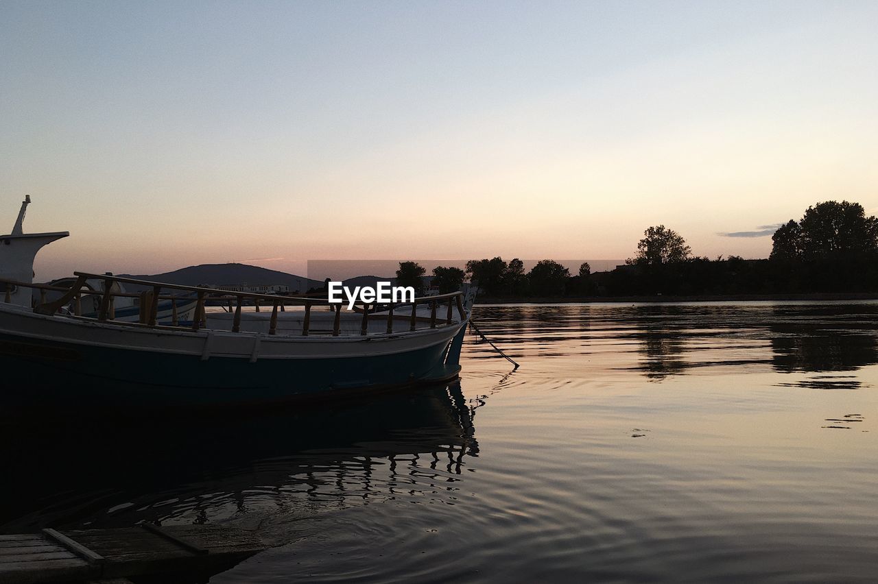 BOAT MOORED IN LAKE AGAINST SKY DURING SUNSET