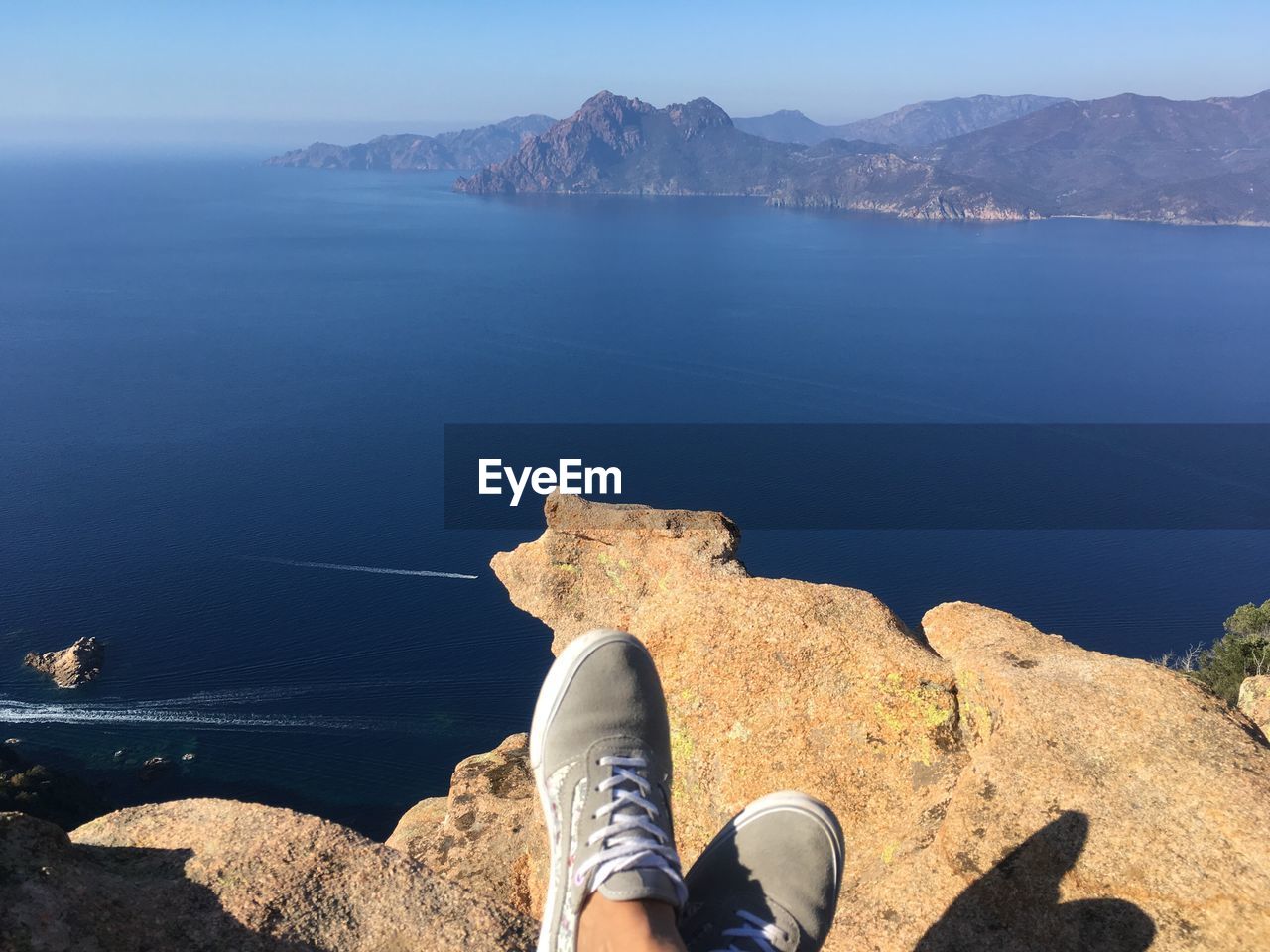 Low section of person wearing shoes on rock against sea