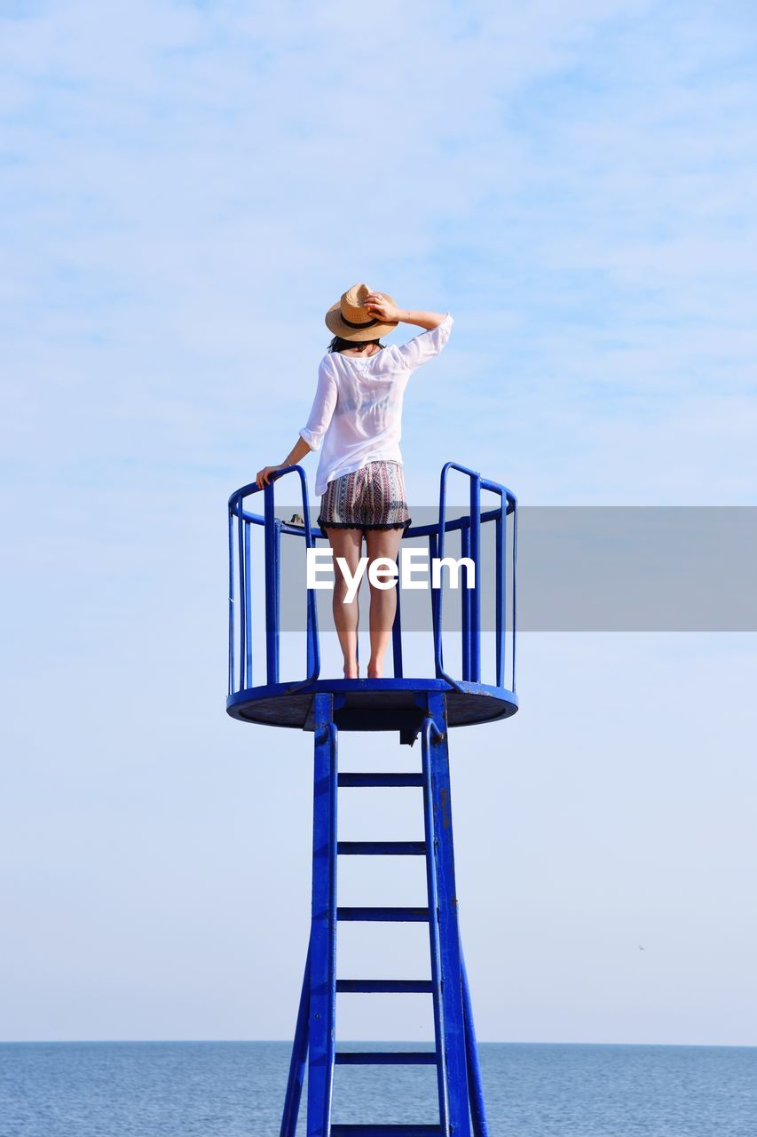Rear view of woman standing on lookout tower looking at sea against sky