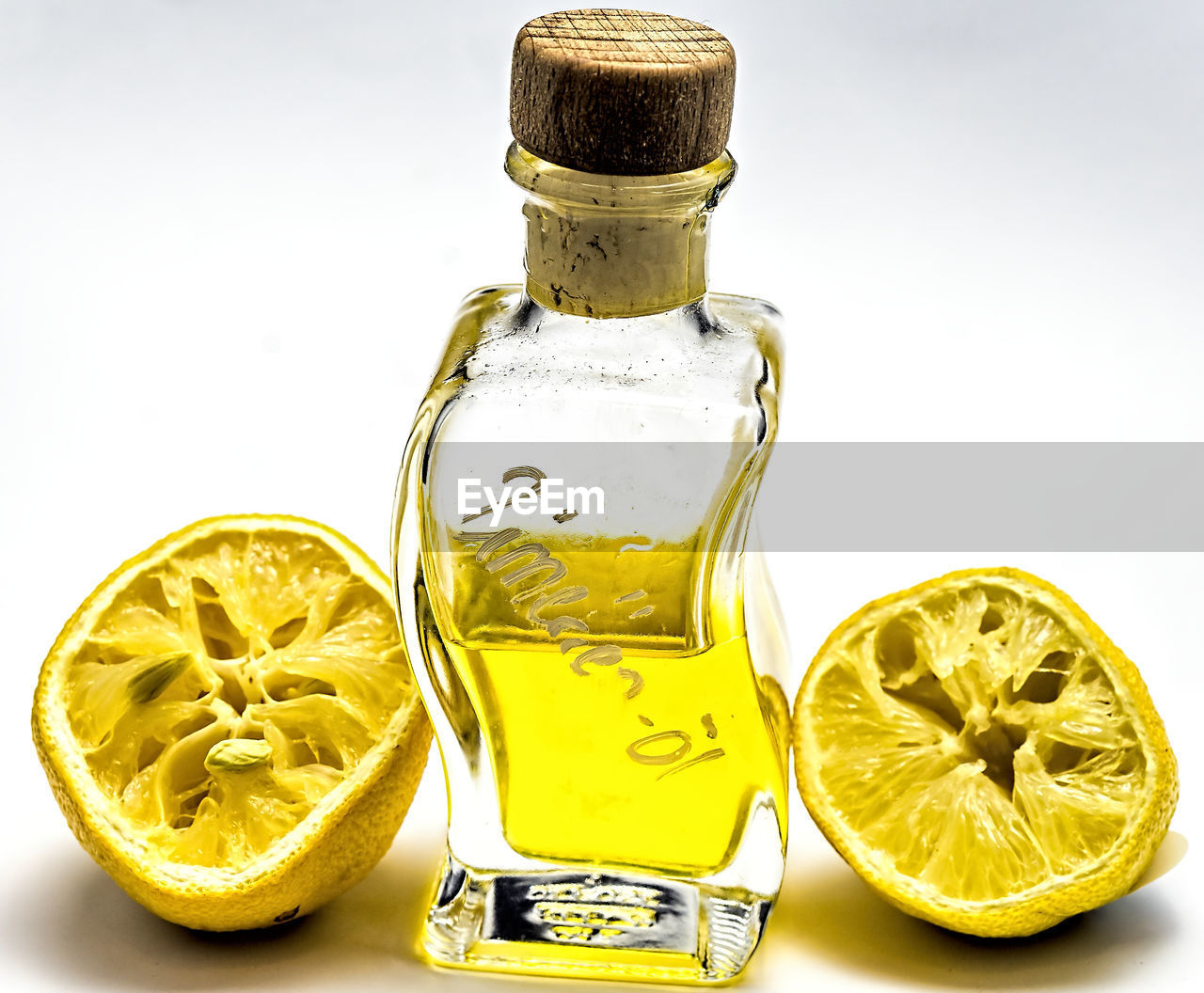 Close-up of lemons and oil in bottle over white background