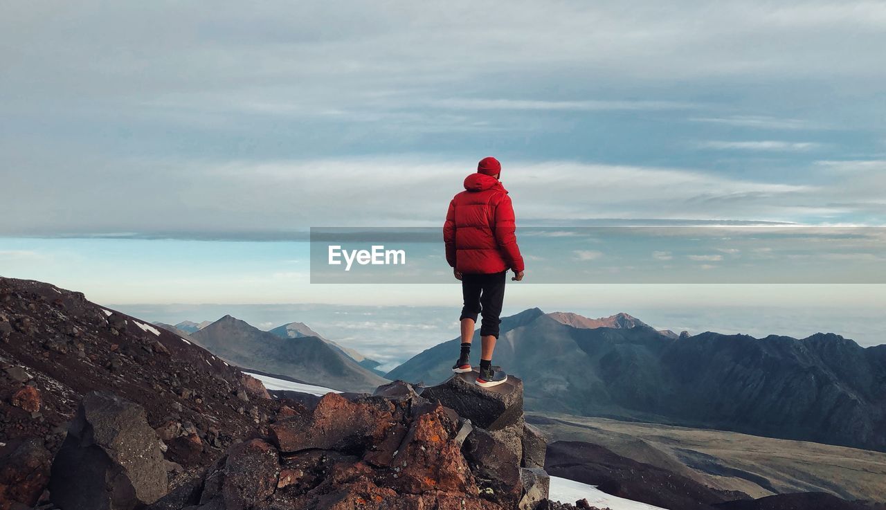 Man standing on rock looking at mountains against sky