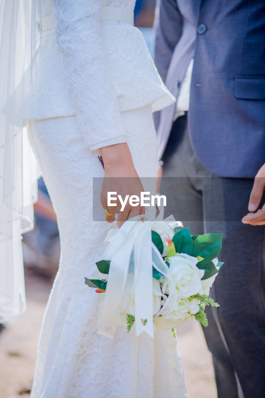 Midsection of bride holding bouquet while standing with groom during wedding ceremony