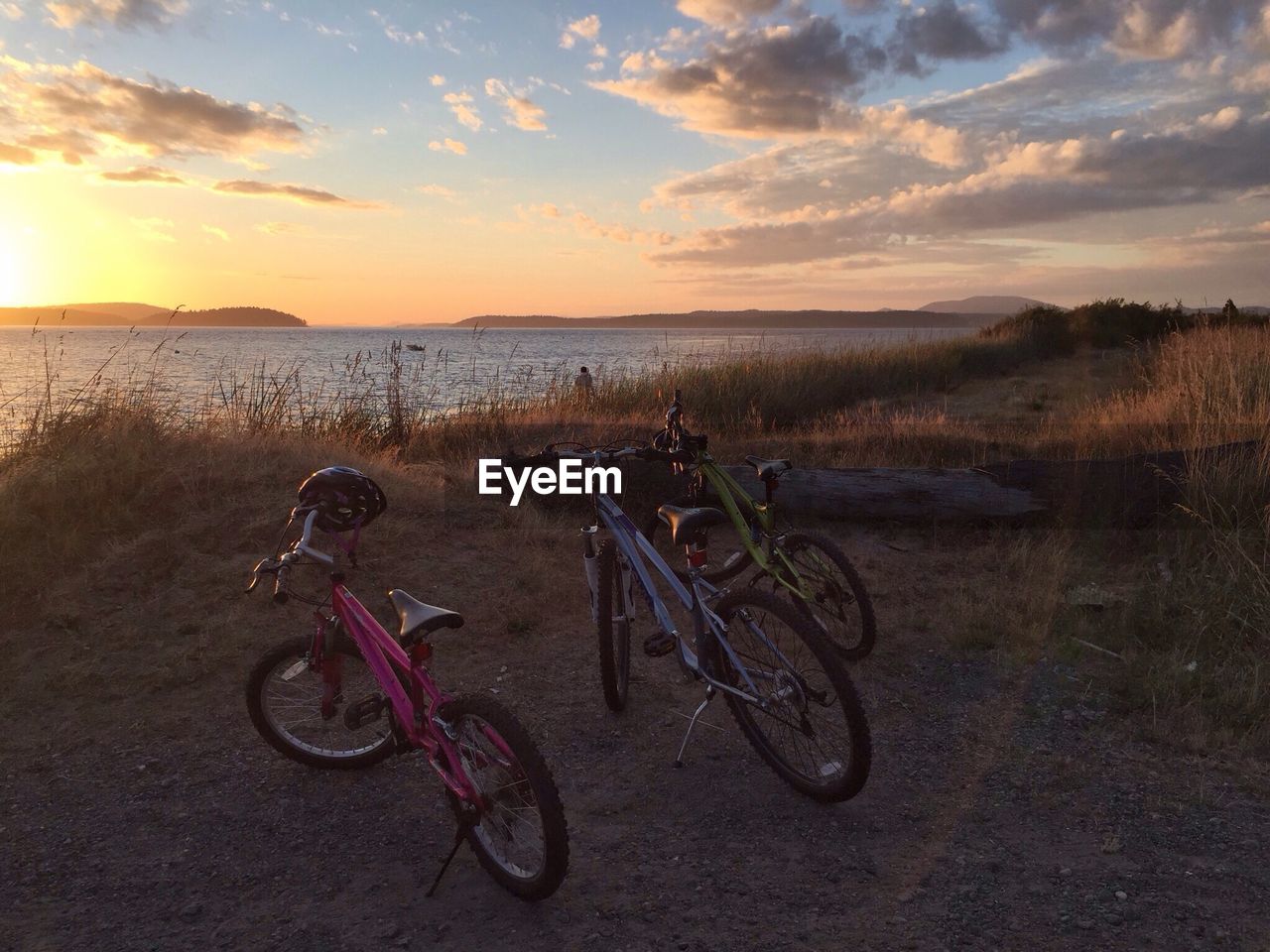 Bicycles parked at lakeshore against sky during sunset