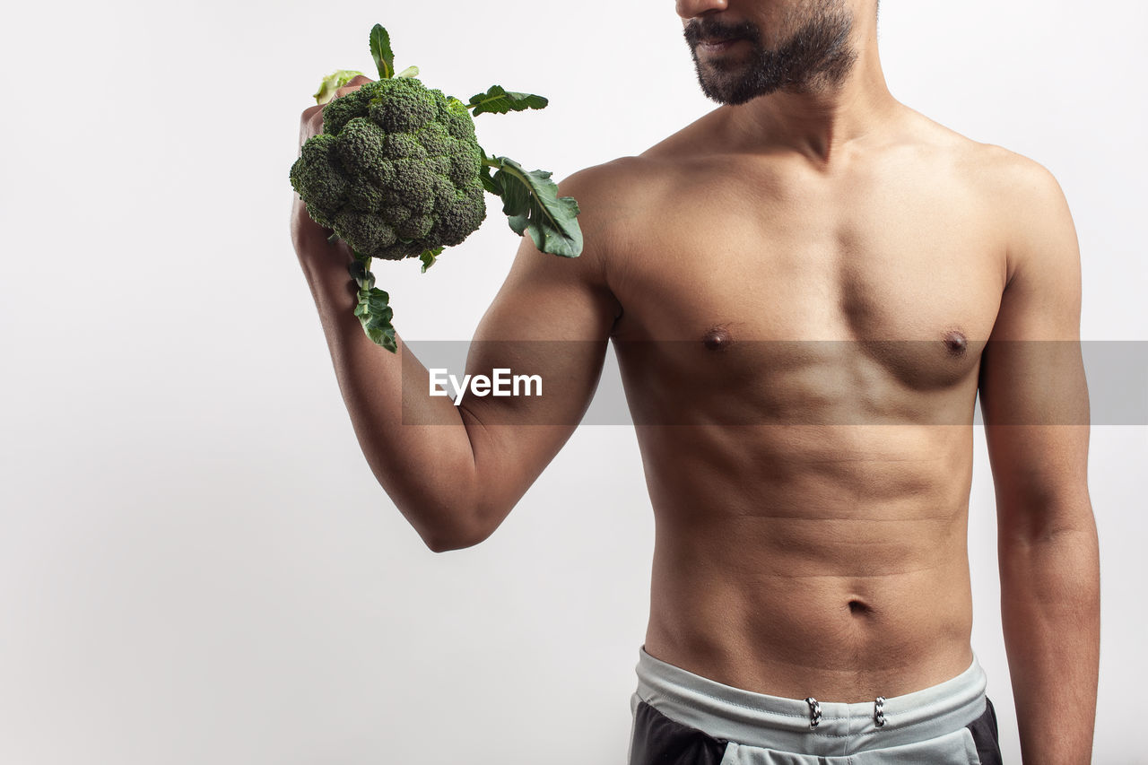 wellbeing, healthy eating, men, food, vegetable, food and drink, studio shot, adult, one person, person, arm, muscular build, freshness, barechested, clothing, indoors, broccoli, waist up, young adult, dieting, standing, portrait, strength, lifestyles, cut out, holding, white background, copy space, root vegetable, organic, human face, torso, human hair, raw food, facial hair