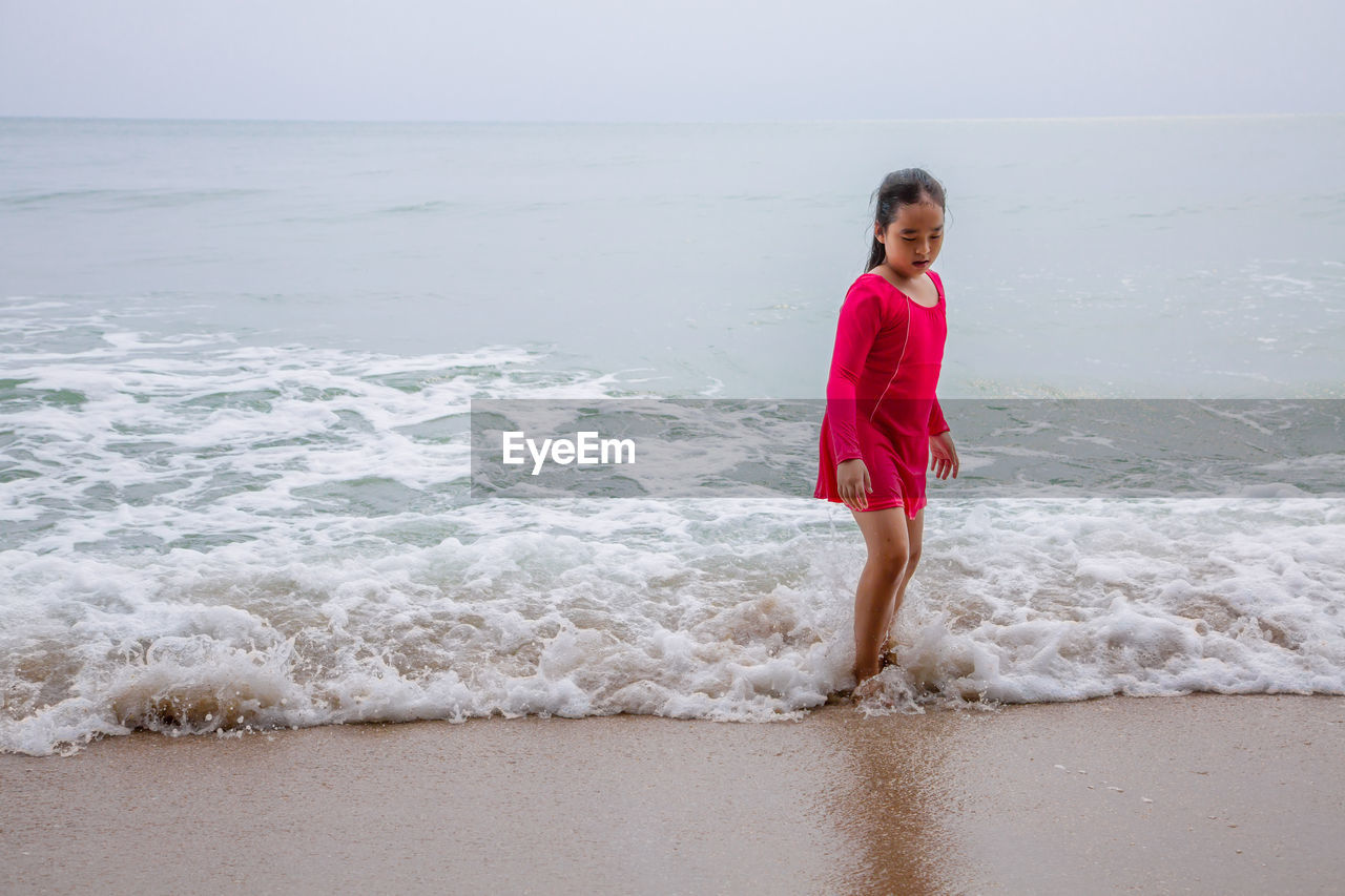 GIRL STANDING ON BEACH AGAINST SKY