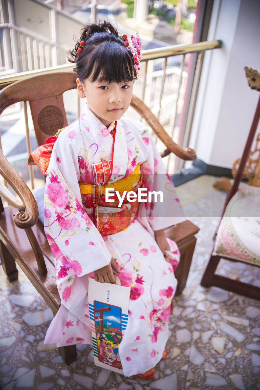 Cute girl in kimono sitting on chair at home