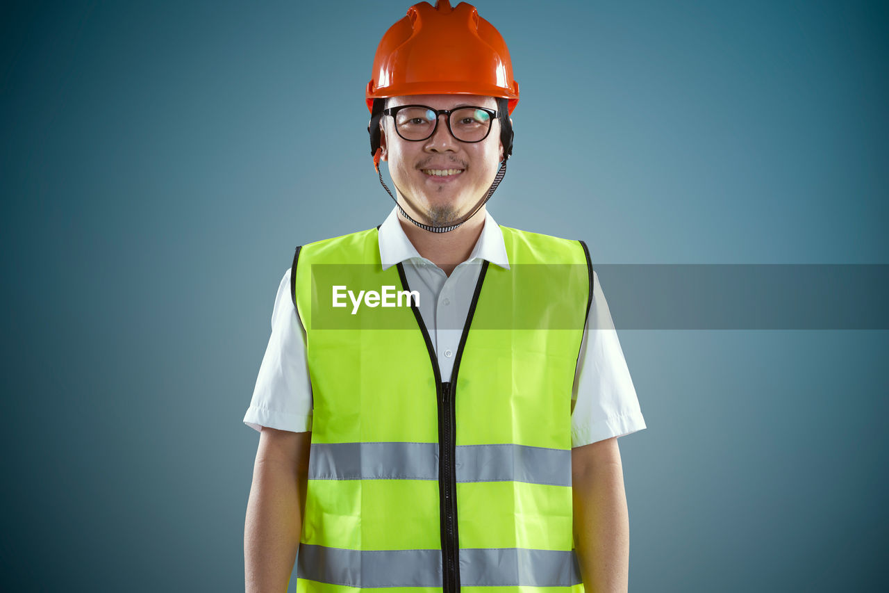 Portrait of smiling construction worker standing against colored background