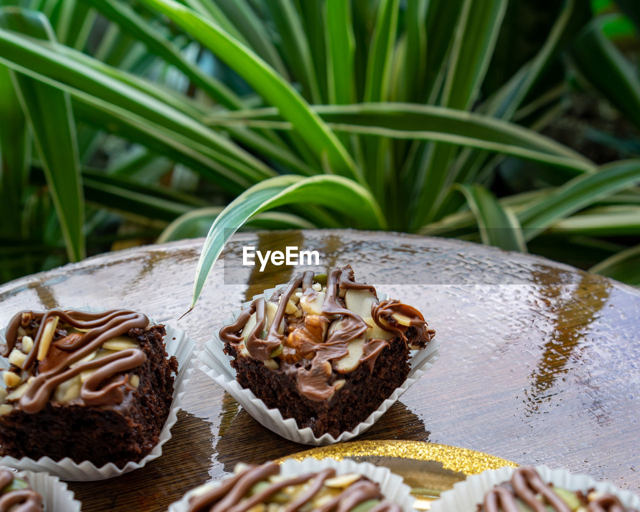 Chocolate brownie cubes with chocolate drizzle in paper cups on a wooden background.