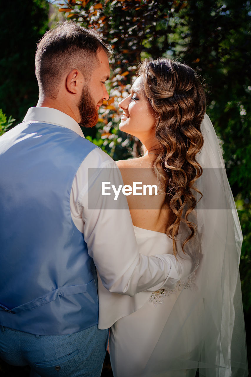 MIDSECTION OF COUPLE HOLDING HANDS STANDING AGAINST BUILDING