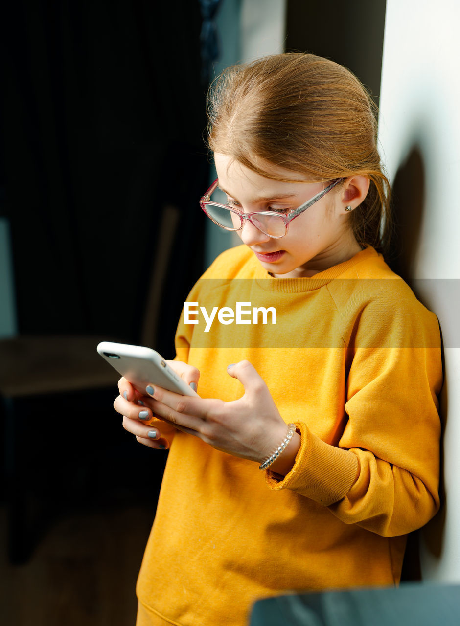 Girl using smart phone against wall