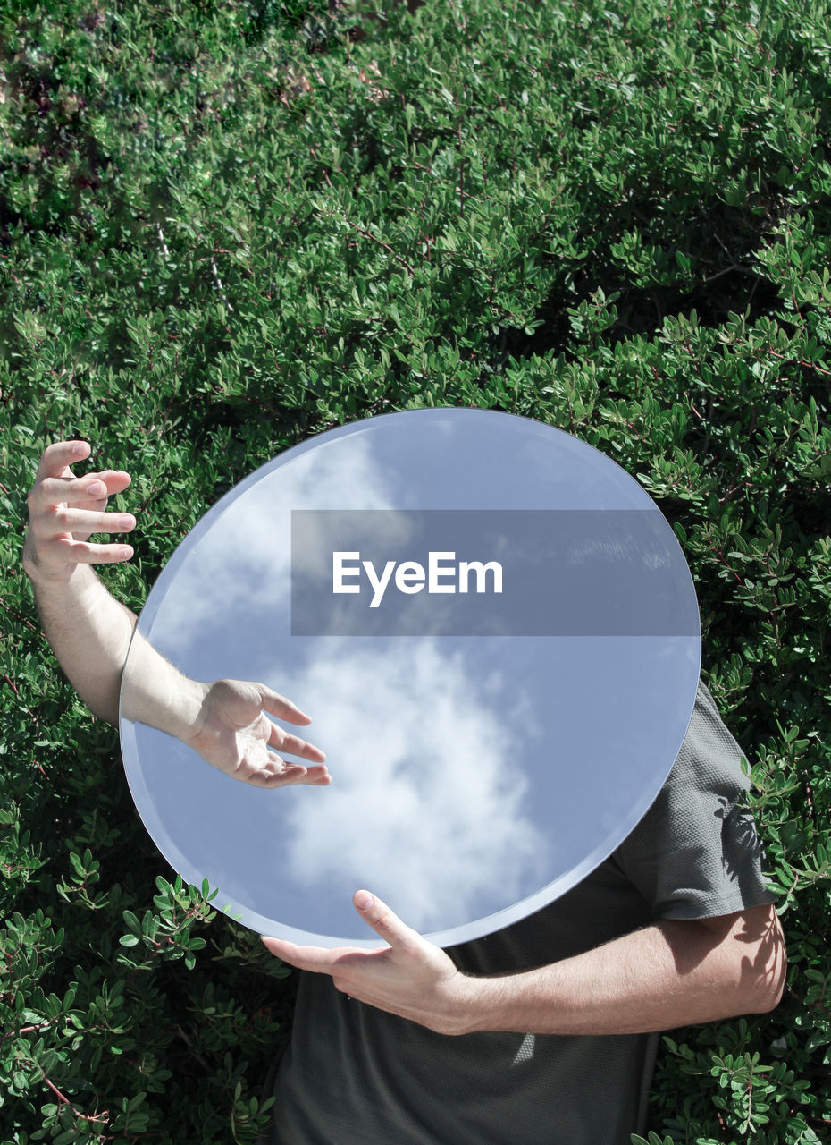 High angle view of man covering face with mirror while standing on field