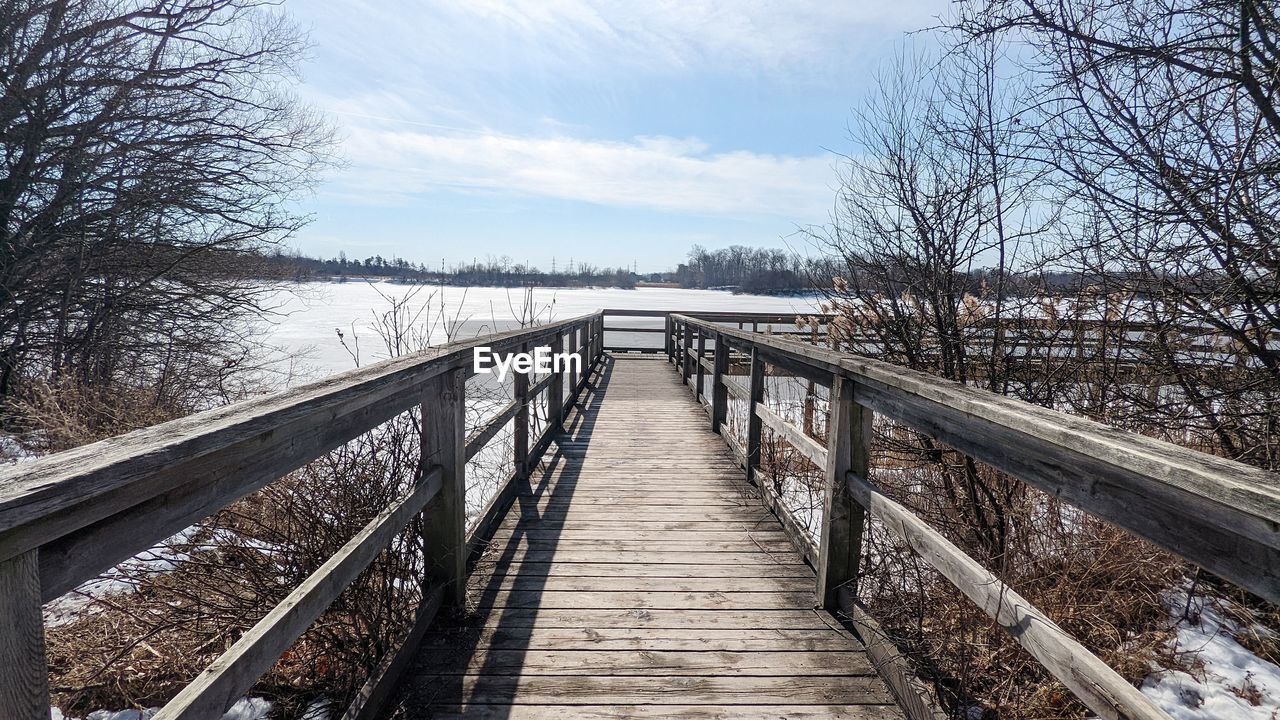 tree, bridge, winter, sky, nature, bare tree, plant, track, the way forward, architecture, water, transport, railing, wood, no people, built structure, walkway, scenics - nature, snow, cloud, footbridge, tranquility, day, diminishing perspective, forest, land, transportation, cold temperature, beauty in nature, footpath, tranquil scene, non-urban scene, outdoors, boardwalk, landscape, river, environment, travel destinations, travel, waterway