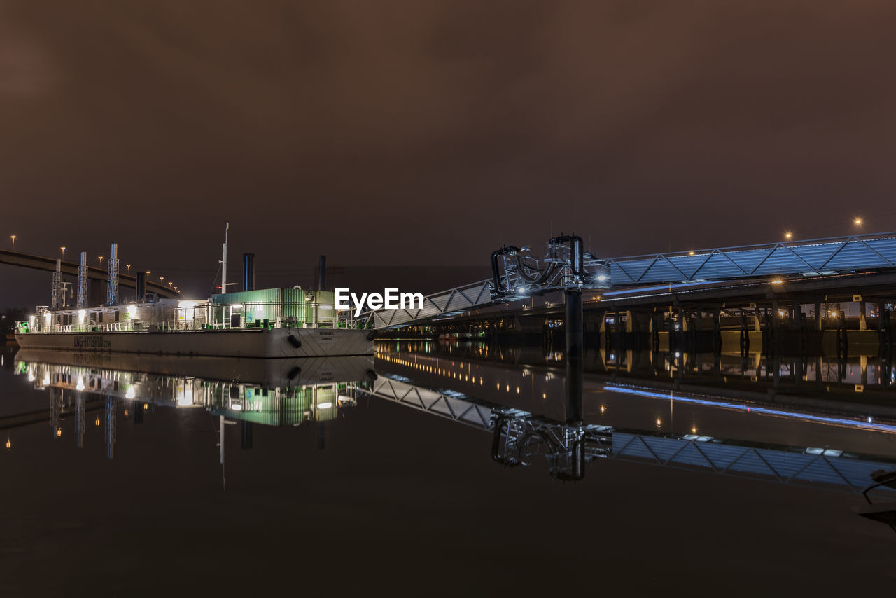 ILLUMINATED BRIDGE OVER RIVER AGAINST SKY