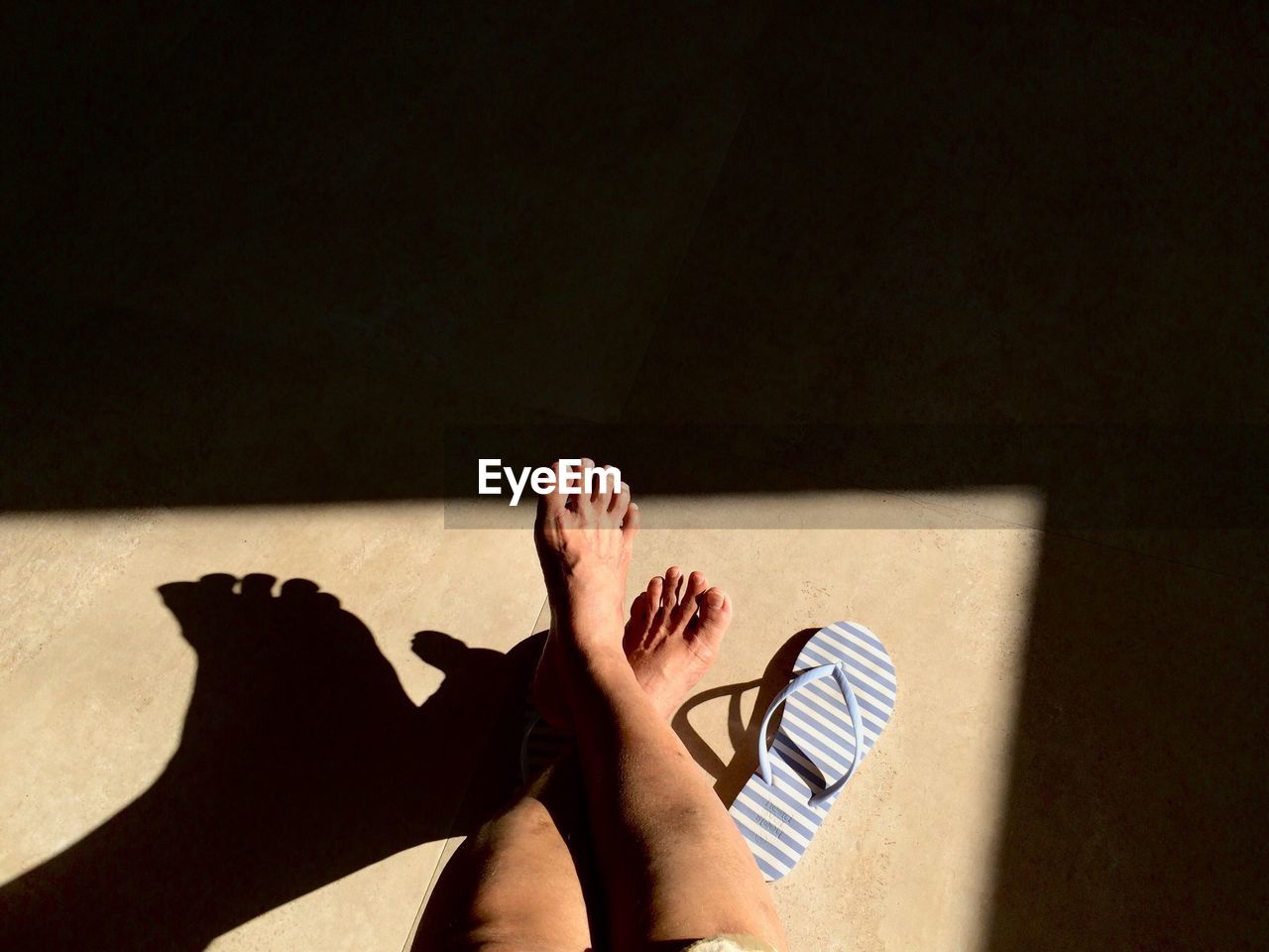 Low section of woman relaxing on floor during sunny day